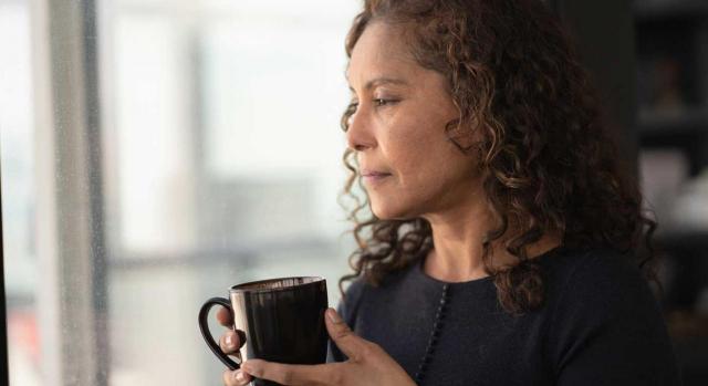 Prestación en favor de familiares. Mujer con una taza en la mano mirando a través de la ventana 