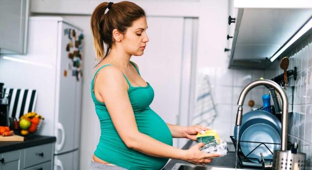 Prestación por maternidad. Mujer embarazada fregando un vaso