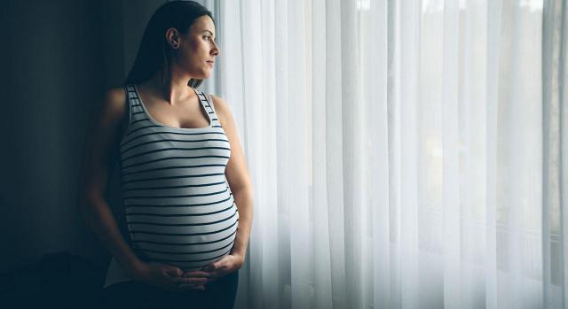 Es discriminatorio no formalizar el contrato de trabajo de una mujer embarazada a la que se le anula el llamamiento para cubrir una vacante temporal por ser dada de baja el día que debía incorporarse. Imagen de mujer embarazada sosteniendo su tripa mientras mira por una ventana