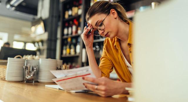 TS. Empresa que da ocupación a tiempo parcial a una trabajadora perceptora de prestaciones de desempleo antes de cursar su alta en seguridad social. ¿La infracción es grave o muy grave? Imagen de una chica en una barra de bar viendo facturas con cara de preocupación