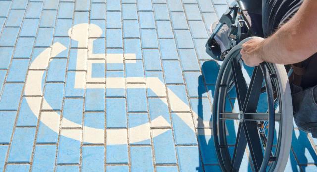 Proceso selectivo por el turno de discapacitados en el sector público. Imagen del logo de una silla de ruedas en el suelo y al lado un chico en silla de ruedas