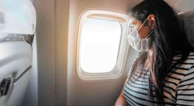 Prórroga de restricción temporal de viajes no imprescindibles desde terceros países a la UE por la COVID-19. Imagen de una chica con mascarilla mirando por la ventanilla de un avión