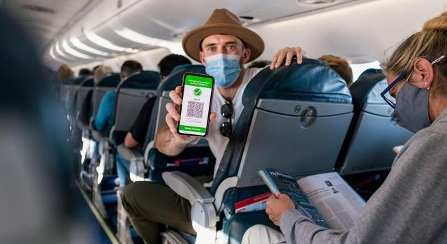 Prórroga de restricciones sin comprobaciones previas en los controles sanitarios. Imagen de un chico con sombrero en un avión mostrando su certificado covid en el móvil  