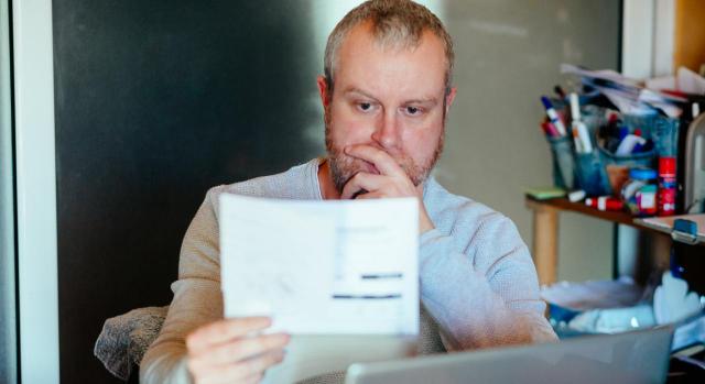 La empresa está obligada a reseñar en las nóminas, respecto a conceptos como «variable vacaciones» y «atrasos». Imagen de un hombre mirando una factura en su casa con cara de preocupación