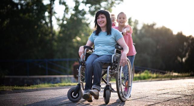 Mujeres con reducción de jornada por cuidado de menor. Imagen de una mujer en silla de ruedas y su hija pequeña empujandola por el parque