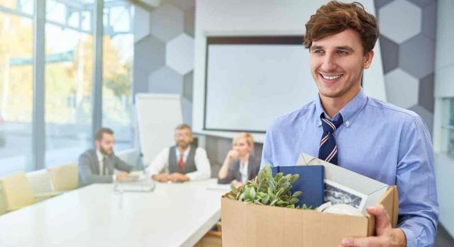 Un trabajadpr, se marcha de la oficina sonriente con una caja en las manos llena de sus cosas