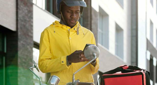 Al FOGASA ya le consta perfectamente el identificador fiscal que aparece como NIE en la TIE. Joven afroamericano con uniforme de mensajero y casco usando un teléfono inteligente