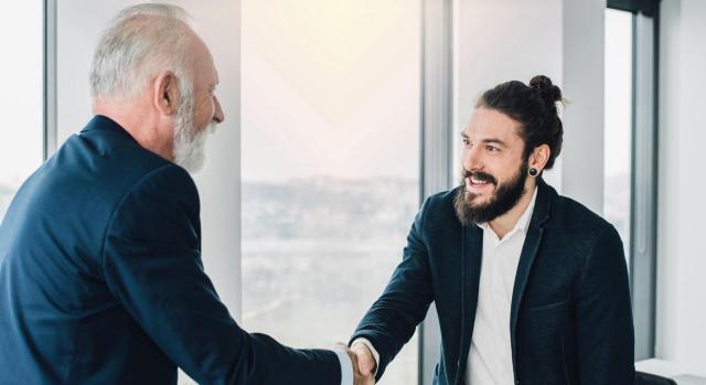 Compañeros de trabajo de diferentes edades estrechándose la mano en la oficina