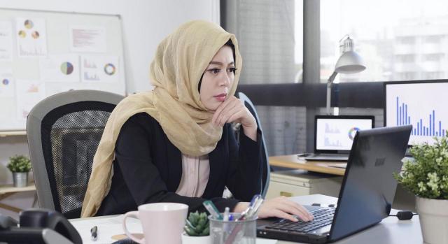 Una administración pública puede decidir prohibir el uso de símbolos religiosos en el lugar de trabajo a todos sus empleados. Imagen de una mujer islámica mirando muy seria un ordenador