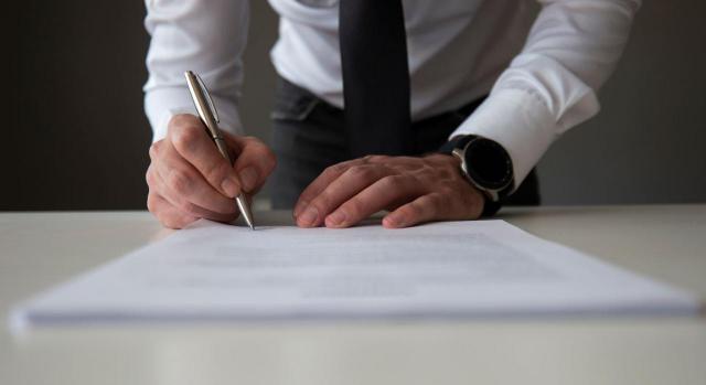 El cambio de titular de una notaría española puede constituir transmisión de empresa. Imagen de una persona con corbata firmando un papel