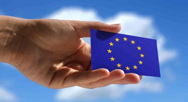 Tarjeta Azul-UE. Primer plano de una mano sosteniendo una Tarjeta Azul-UE con un cielo azul y nubes de fondo