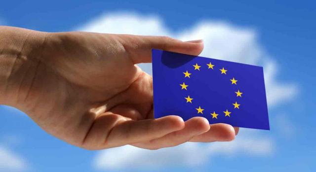 Tarjeta Azul-UE Tarjeta Azul-UE. Primer plano de una mano sosteniendo una Tarjeta Azul-UE con un cielo azul y nubes de fondo