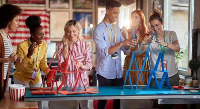 Ventajas e inconvenientes del team building: ¿Es realmente beneficioso para tu empresa? Imagen de dos grupos de jovenes haciendo torres de papel