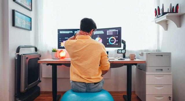 Teletrabajo. Obligación de la empresa de proporcionar a los trabajadores una silla ergonómica. Imagen de un chico teletrabajando encima de una bola azul de pilates