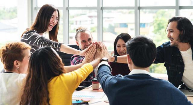 Trabajadores motivados. Imagen de un grupo de trabajadores multiétnico chocando manos y riendo en reunión brainstorm en oficina