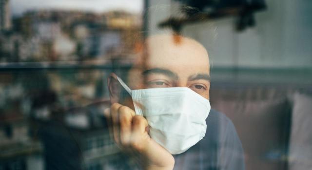 Pandemia de COVID-19: el Derecho de la Unión no exige que un empleado que haya tenido que guardar cuarentena durante sus vacaciones anuales retribuidas pueda aplazar estas. Imagen de un hombre con mascarilla mirando por una ventana