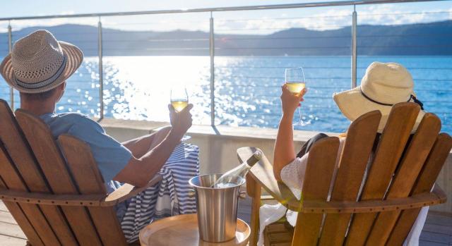 La fijación de un periodo de aplazamiento para el disfrute de vacaciones anuales retribuidas. Imagen de una pareja en tumbonas, tomanddo vino mirando hacía un lago