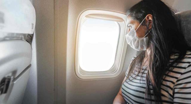 viajes covid19. Chica con mascarilla mirando a través de la ventanilla de un avión