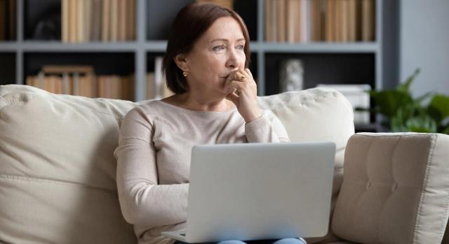 Debe aplicarse la norma de forma flexible. Mujer de mediana edad pensativa sentada con portátil sobre rodillas